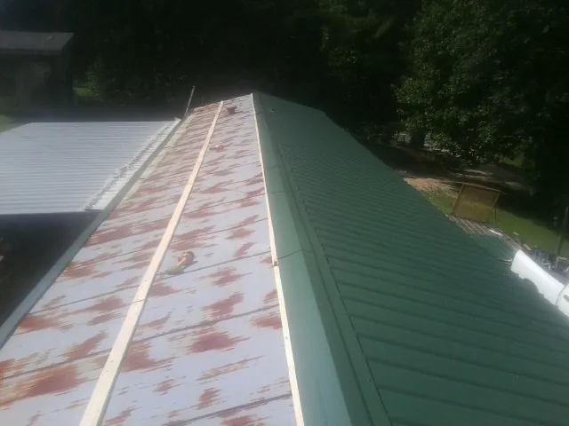 Old rusted panels beside newly installed green metal roofing — Wind Damage Roof Repair by Roofing Brothers in Lansing