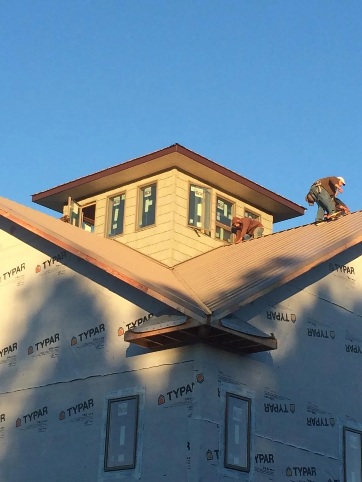 Roofers working around a rooftop cupola on a new metal roof at sunset — Roof Waterproofing in Lansing by Roofing Brothers
